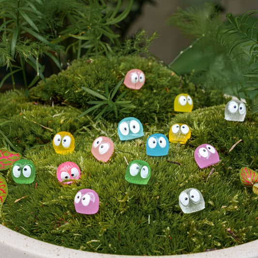 Kleine, kleurrijke plastic speelgoedfiguren met grote ogen rusten op groen mos, perfect voor decoratie in een tuin of als speelgoed voor kinderen. Ideaal voor creatieve tuinprojecten en speelplekken.