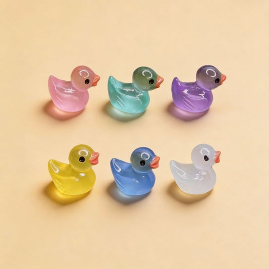 Kleine glazen eendjes in kleuren zoals roze, groen, blauw, geel en paars staan op groen mos in een pot. Perfect als decoratie voor een tuin of als speelgoed voor kinderen.