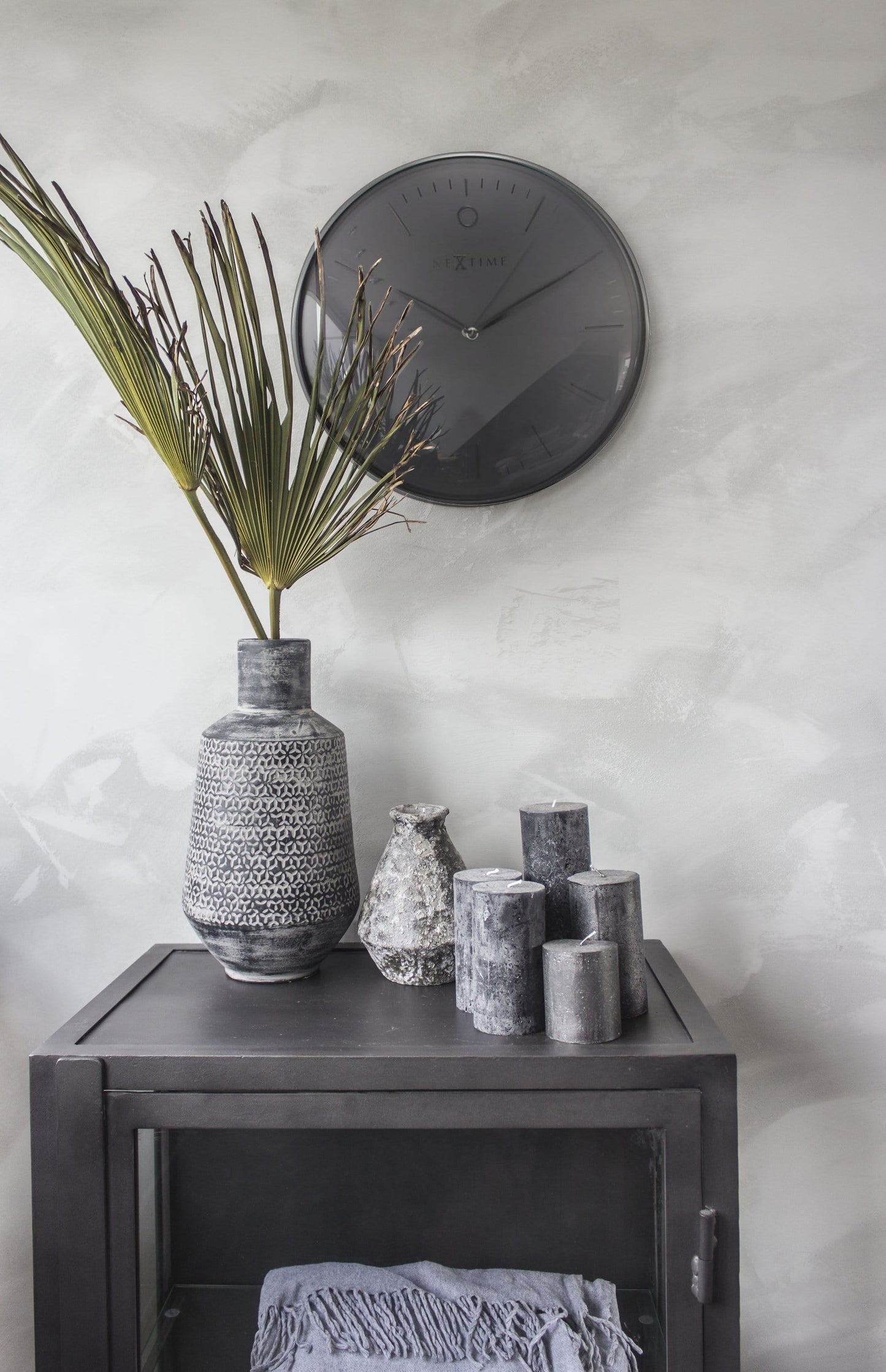 Een minimalistische, zwarte wandklok van Nextime met een mat zwart wijzerplaat en dunne zilverkleurige wijzers. Geschikt voor moderne interieurs en als decoratief element in woon- of kantoorruimtes.