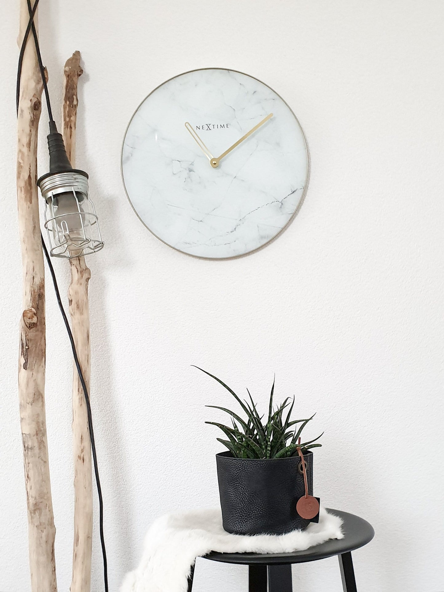 Een elegante wandklok met wit marmeren oppervlak en goudkleurige wijzers. De klok heeft een dunne gouden rand en het merk 'NEXTIME' in het midden, geschikt voor moderne interieurs.