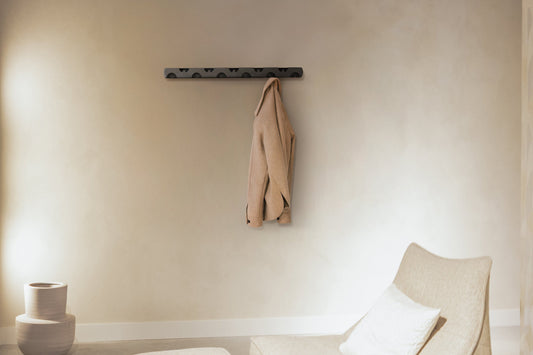 Een minimalistisch zwart wandkoord met vijf haken, waarop een beige wollen jas hangt. Geschikt voor moderne interieurs en praktisch voor kleding opbergen in woon- of entreezones.