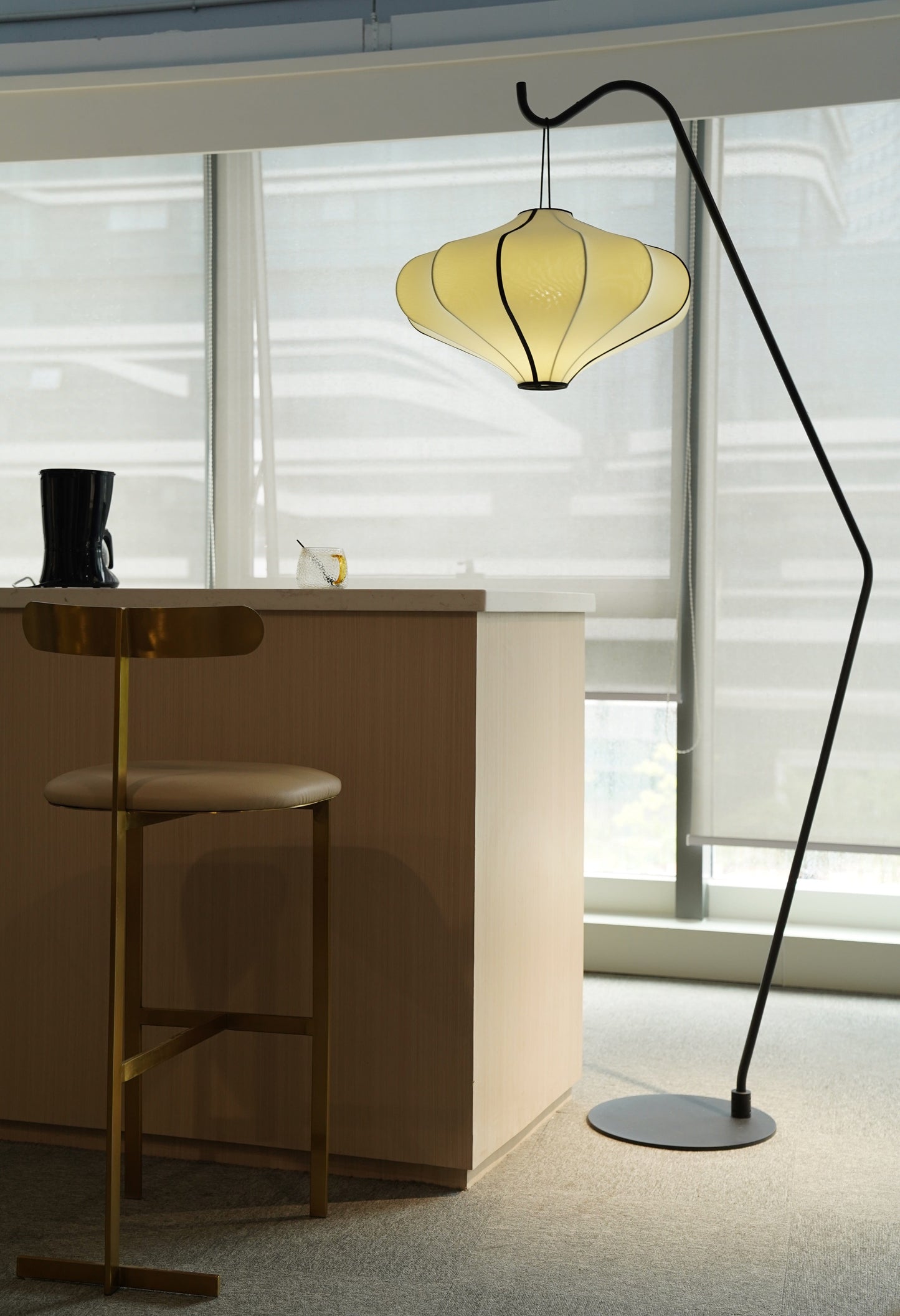 Een zwart, minimalistisch vloerlampenstel met een gebogen metalen arm en een ronde voet, waarop een witte, gestileerde lichtkap hangt. Ideaal voor moderne interieurs en als decoratieve verlichting in woon- of werkkamers.