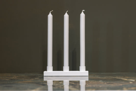 Een minimalistisch zwart kaarsenhouder met drie witte kaarsen, geplaatst op een marmeren oppervlak. Ideaal voor een moderne, rustige sfeer in woon- of eetkamer.