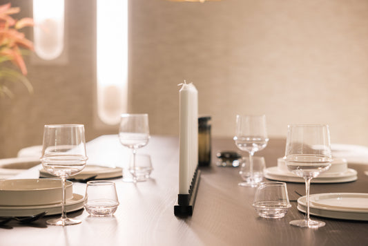 Een elegante tafelsetting met witte porseleinen borden, glazen en een zwart kandelaar met witte kaarsen, perfect voor een romantisch diner of feestelijke avond.