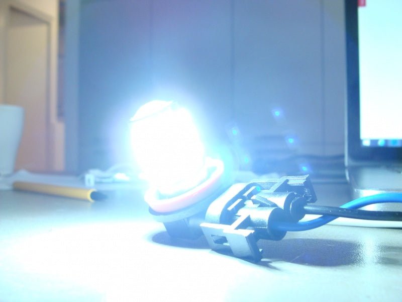 Blauwe T10 LED-lamp met vier gele chiplichtbronnen en zichtbare elektronische componenten, geschikt voor auto- en motorvoertuigen. Zichtbare kabels en metalen contactpunten voor eenvoudige installatie.