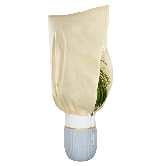 Een crèmekleurige, waterafstotende plantenkap met rits en trekkoord, bedekt een groene kamerplant in een grijze pot. Ideaal voor binnen- en buitenruimtes, bescherming tegen zon en regen.