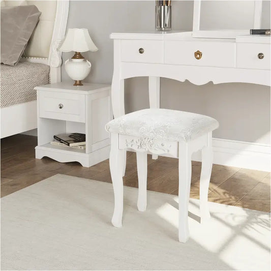 Een witte, klassieke houten kruk met gedetailleerde bloemversiering en een gestoffeerd zitvlak met zichtbare kant. Perfect voor een elegante make-up of schoenenstijl in een slaapkamer.