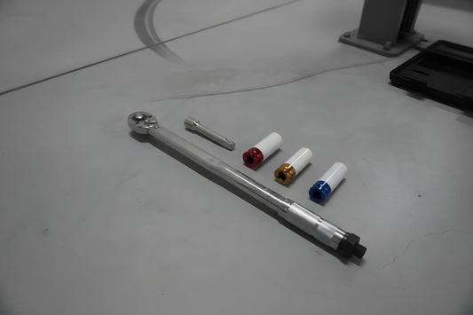 Zilverkleurige schroefspanner in zwarte houder, met kleurrijke (blauw, geel, rood) aanpasbare koppen. Geschikt voor precisie-schroefwerk in auto’s en machines.