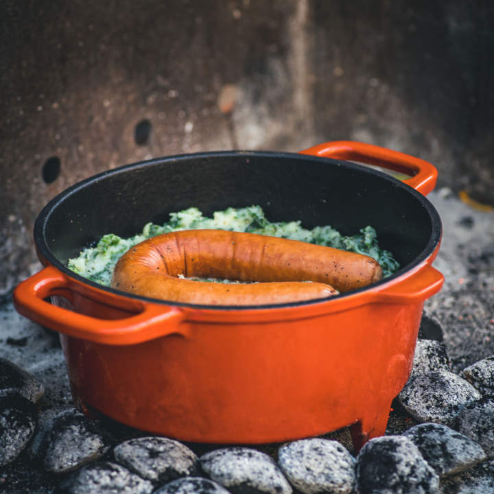 Oranje kookpot met afdekking van The Windmill, een beperkte editie gietijzerpot met glazuur, geschikt voor kampvuur of hoge hitte. Perfect voor buitenkoken en grillen.