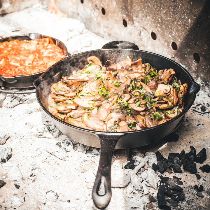 Een zwarte, glanzende kookpan van gietijzer met een lang handvat en een klein handvat aan de zijkant, geschikt voor grillen en bakken op elke kookplaat.