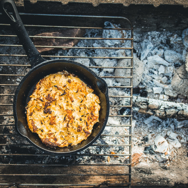 Zwarte kookpan van gietijzer met gladde, glazuurloze binnenkant en een lang, gebogen handvat. Geschikt voor grillen en bakken op hoge temperaturen.