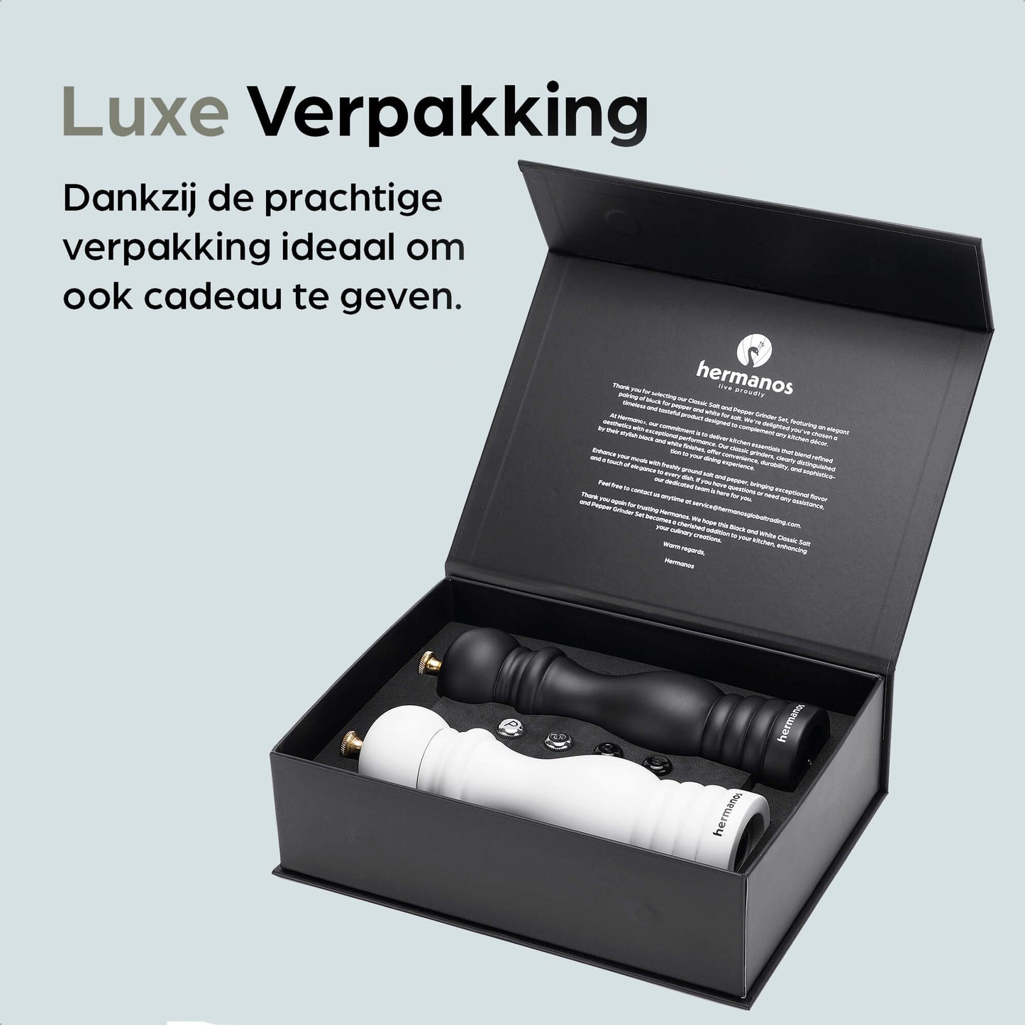 Een witte en zwarte houten pepermolen met goudkleurige doppen, geplaatst op een zwarte standaard met het merk 'hermanos'. Inclusief extra zilveren doppen voor keuken- en eetkamerdecoratie.