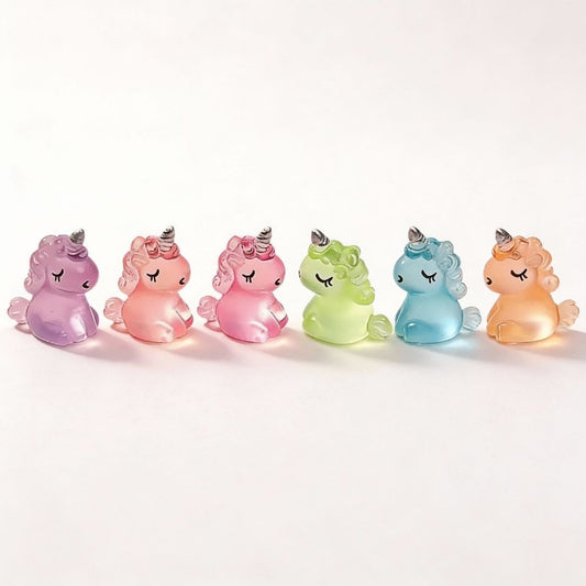 Zes kleurrijke glazen eenhoorns in pastelkleuren, elk met een zilveren hoorn en gesloten ogen, perfect als decoratie voor kinderkamer of als speelgoed voor jonge kinderen.
