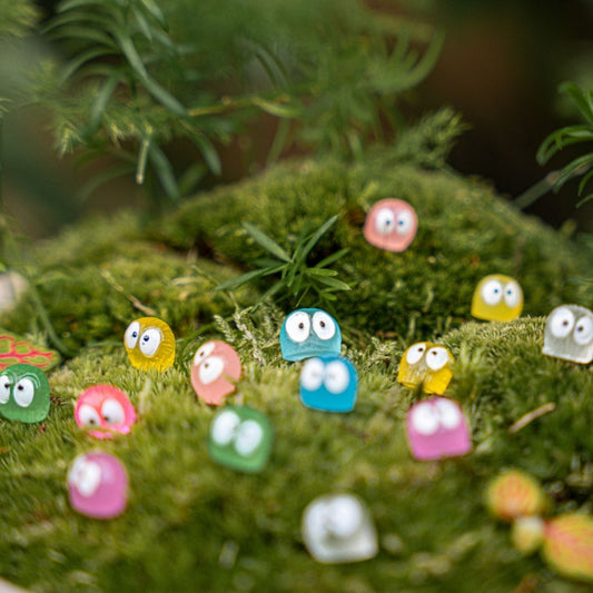 Kleine, kleurrijke plastic speelgoedfiguren met grote ogen rusten op groen mos, perfect voor decoratieve tuin- of binnenlandse sfeer. Ideaal als speelgoed of decoratie voor kinderen en liefhebbers van miniaturen.