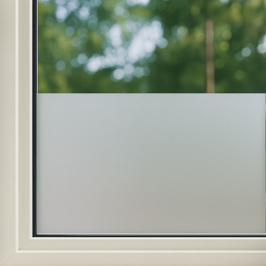 Frosted privacy film op een wit raamkozijn, zacht mat wit met een heldere, groene tuin op de achtergrond. Ideaal voor privacy in woon- en kantoorruimtes.
