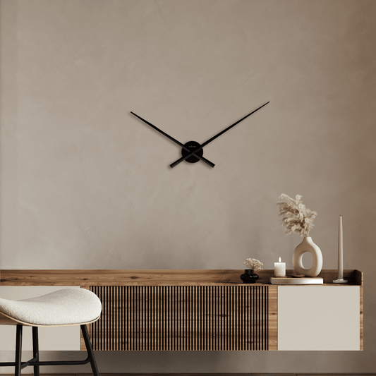 Een minimalistische zwarte wandklok van NEXTIME met dunne wijzers en een ronde basis, geschikt voor moderne interieurs. Perfect voor een stijlvolle kamerdecoratie of als designaccessoire in een woonkamer.