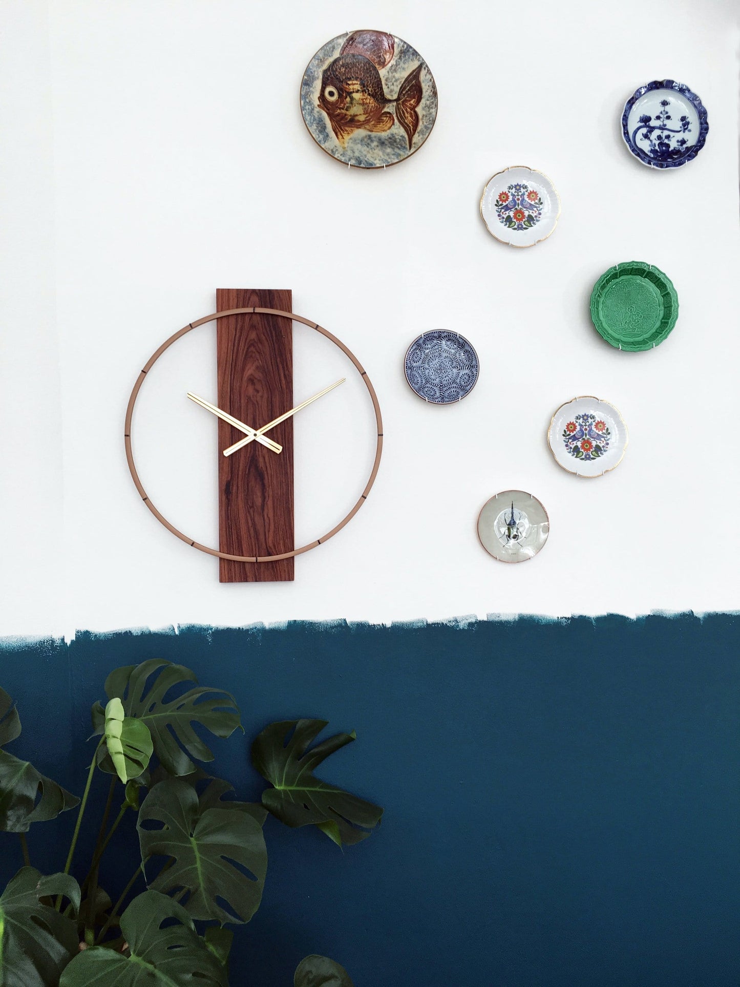 Een moderne wandklok met een goudkleurige metalen ring en een donkerbruine houten plaat met zichtbare grain. De dunne wijzers en het merk 'NEXTIME' zijn duidelijk zichtbaar. Geschikt voor minimalistische interieurs en als decoratief element in woon- of kantoorruimtes.