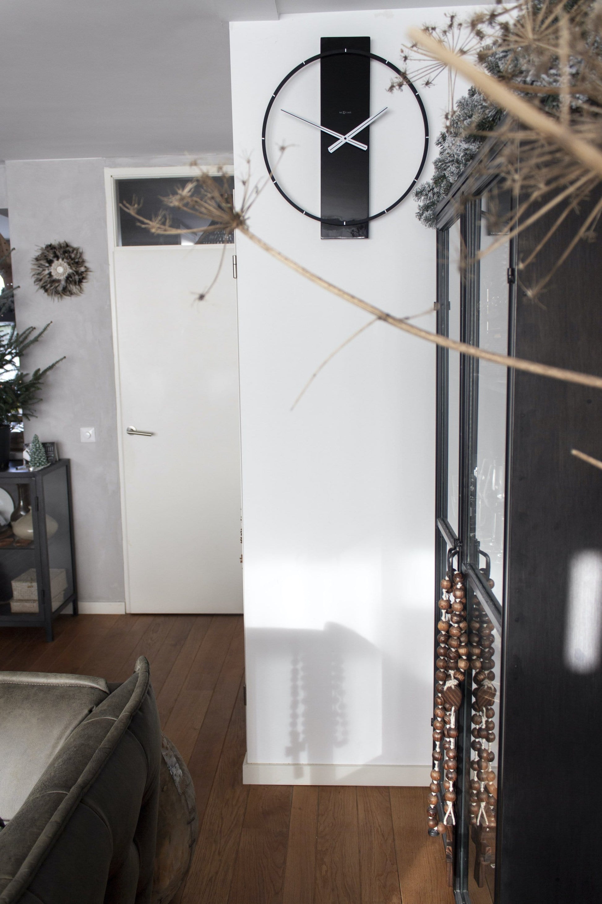 Een moderne, zwarte wandklok van het merk Nextime met een minimalistisch ontwerp, zilverkleurige wijzers en een glanzende, ronde kaderstructuur. Perfect voor een stijlvolle woonkamer of kantoorruimte.