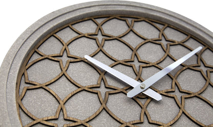 Een moderne wandklok met een grijze betonrand en een houten, geometrisch patroon. Zilverkleurige wijzers en het merk 'NEXTIME' zijn zichtbaar. Geschikt voor minimalistische interieurs en moderne woonkamers.