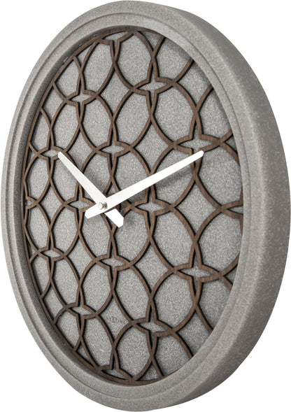 Een moderne wandklok met een grijze betonrand en een houten, geometrisch patroon. Zilverkleurige wijzers en het merk 'NEXTIME' zijn zichtbaar. Ideaal voor minimalistische interieurs of als decoratief element in woon- en werkkamers.