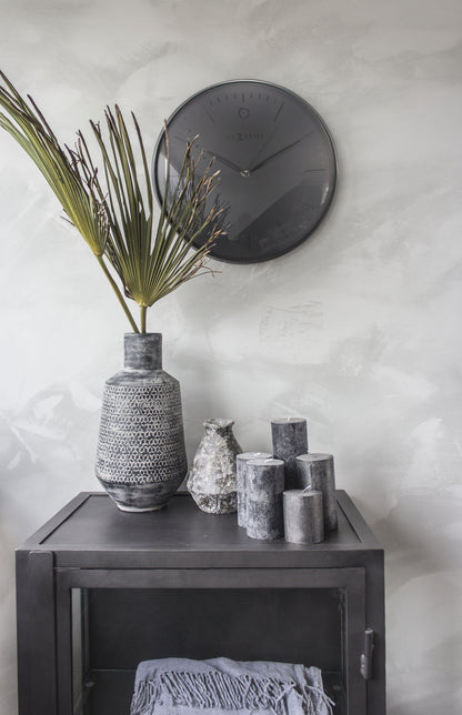 Een minimalistische, zwarte wandklok van Nextime met een mat zwart wijzerplaat en dunne zilverkleurige wijzers. Geschikt voor moderne interieurs en als decoratief element in woon- of kantoorruimtes.