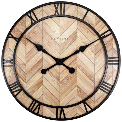 Een ronde wandklok met houten chevronpatroon en zwarte Romeinse cijfers. Zichtbare merknaam ‘NEXTIME’ en elegante wijzers voor moderne interieurs. Perfect voor woonkamer of kantoordecoratie.
