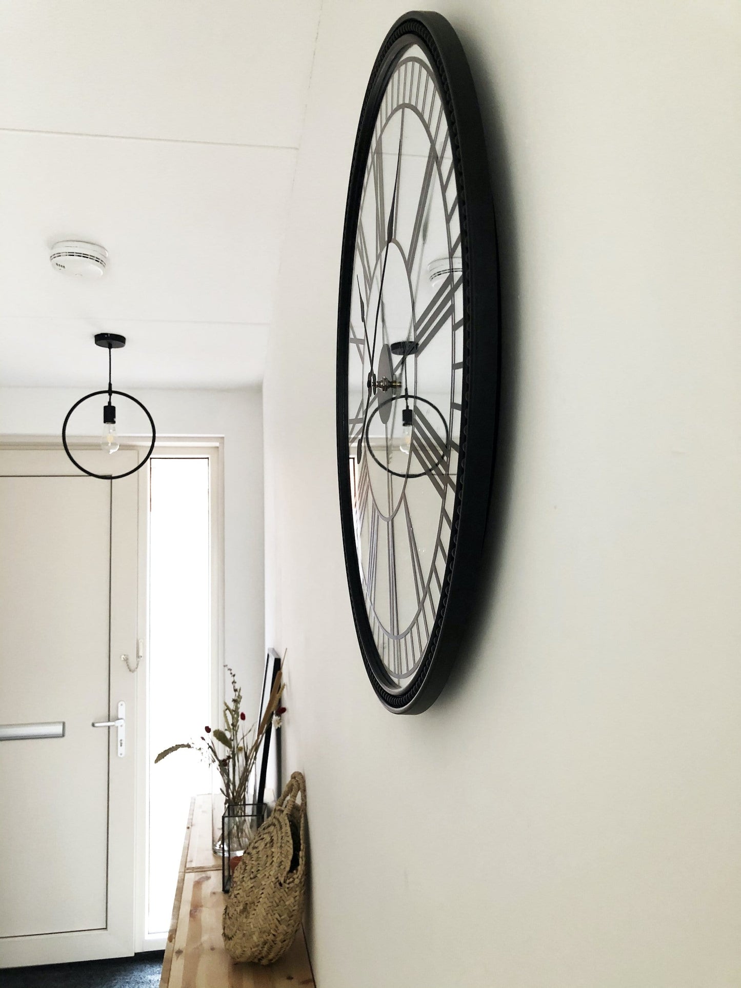 Een klassieke wandklok met zwart metalen kader en witte wijzerplaat met Romeinse cijfers. De klok heeft een elegante, klassieke stijl geschikt voor woonkamer of kantoor.