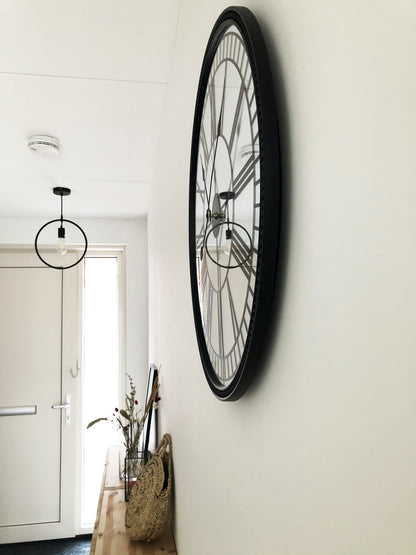 Een klassieke wandklok met zwart metalen kader en witte wijzerplaat met Romeinse cijfers. De klok heeft een elegante, klassieke stijl geschikt voor woonkamer of kantoor.