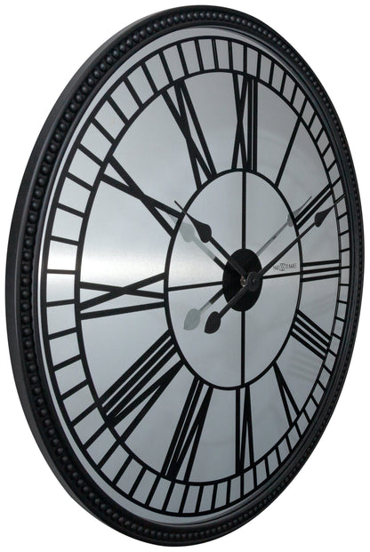 Een klassieke wandklok met zwart metalen kader en witte wijzerplaat met Romeinse cijfers. De wijzers en het merk 'NEXTIME' zijn duidelijk zichtbaar. Geschikt voor woonkamer of kantoordecoratie.