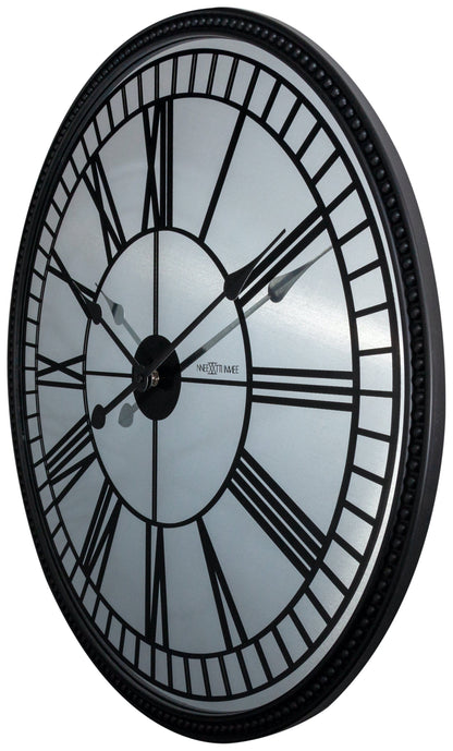 Een klassieke wandklok met zwart metalen kader en witte wijzerplaat met Romeinse cijfers. De wijzers en het merk ‘NEXTIME’ zijn duidelijk zichtbaar, geschikt voor woonkamer of kantoor.