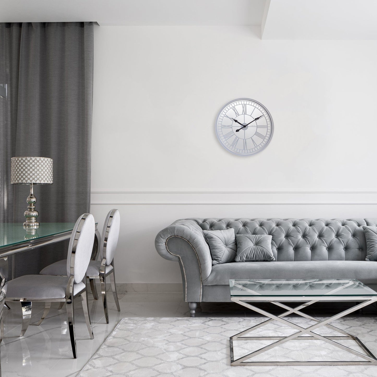 Een elegante, zilverkleurige wandklok met Romeinse cijfers en zwarte wijzers. De klok heeft een glanzende, gepolijste rand en is ideaal voor een moderne woonkamer of kantoorruimte.
