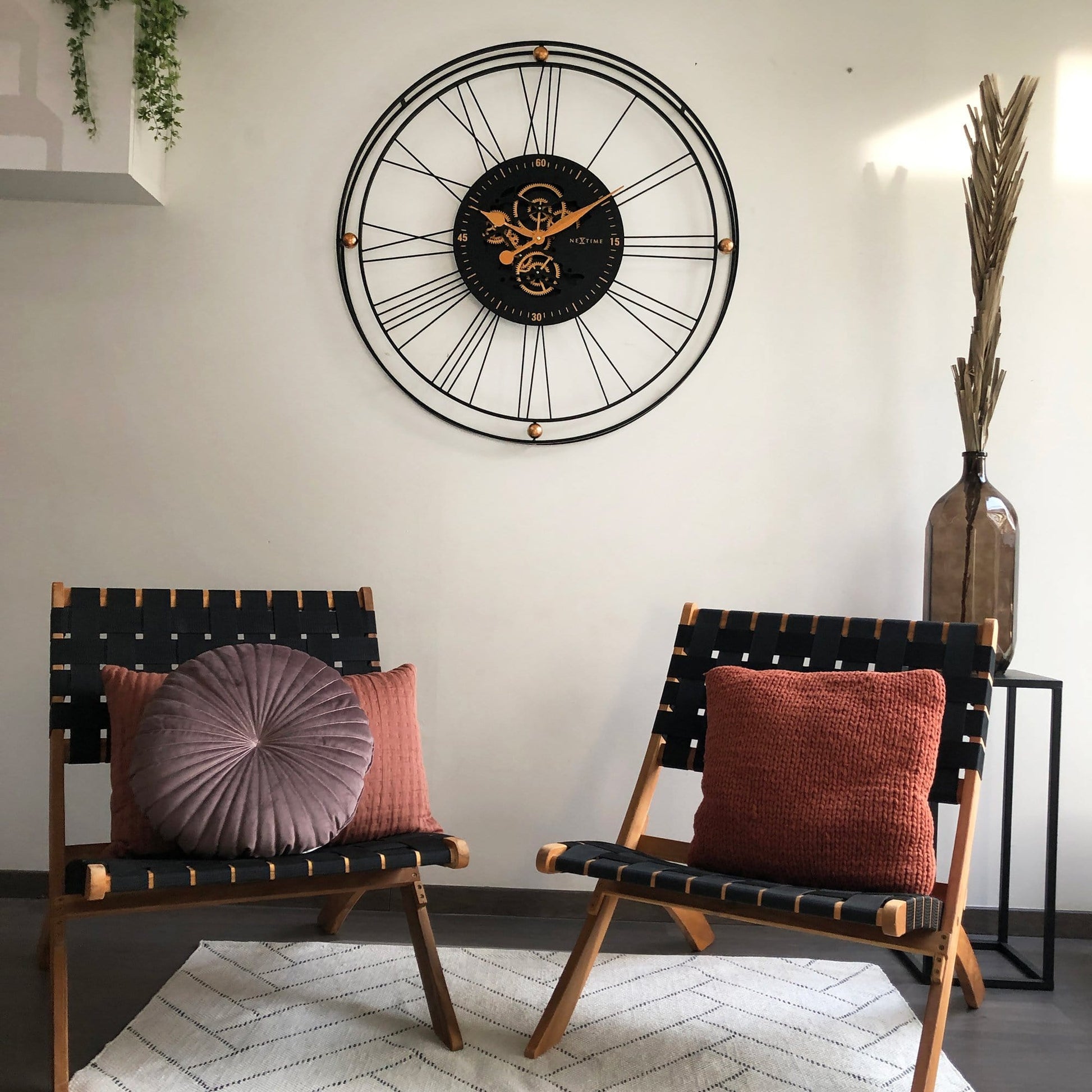 Een industriële wandklok met zwart metaalframe en zichtbare goudkleurige tandwielen, voorzien van drie koperen knoppen. Perfect voor een moderne woonkamer of kantoordecoratie.