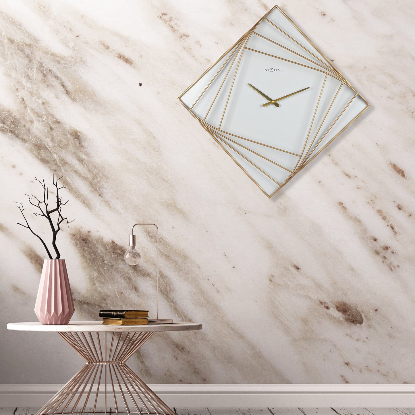 Een elegante, goudkleurige wandklok met geometrisch ontwerp en witte glasvlakken. De minimalistische klok heeft dunne wijzers en het merk 'NEXTIME' zichtbaar, geschikt voor moderne interieurs.
