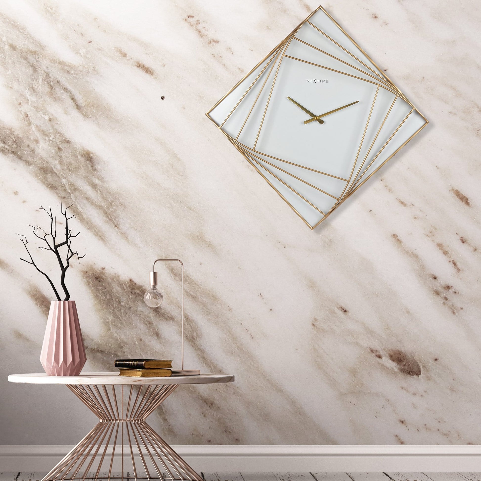 Een elegante, goudkleurige wandklok met geometrisch ontwerp en witte glasvlakken. De minimalistische klok heeft dunne wijzers en het merk 'NEXTIME' zichtbaar, geschikt voor moderne interieurs.
