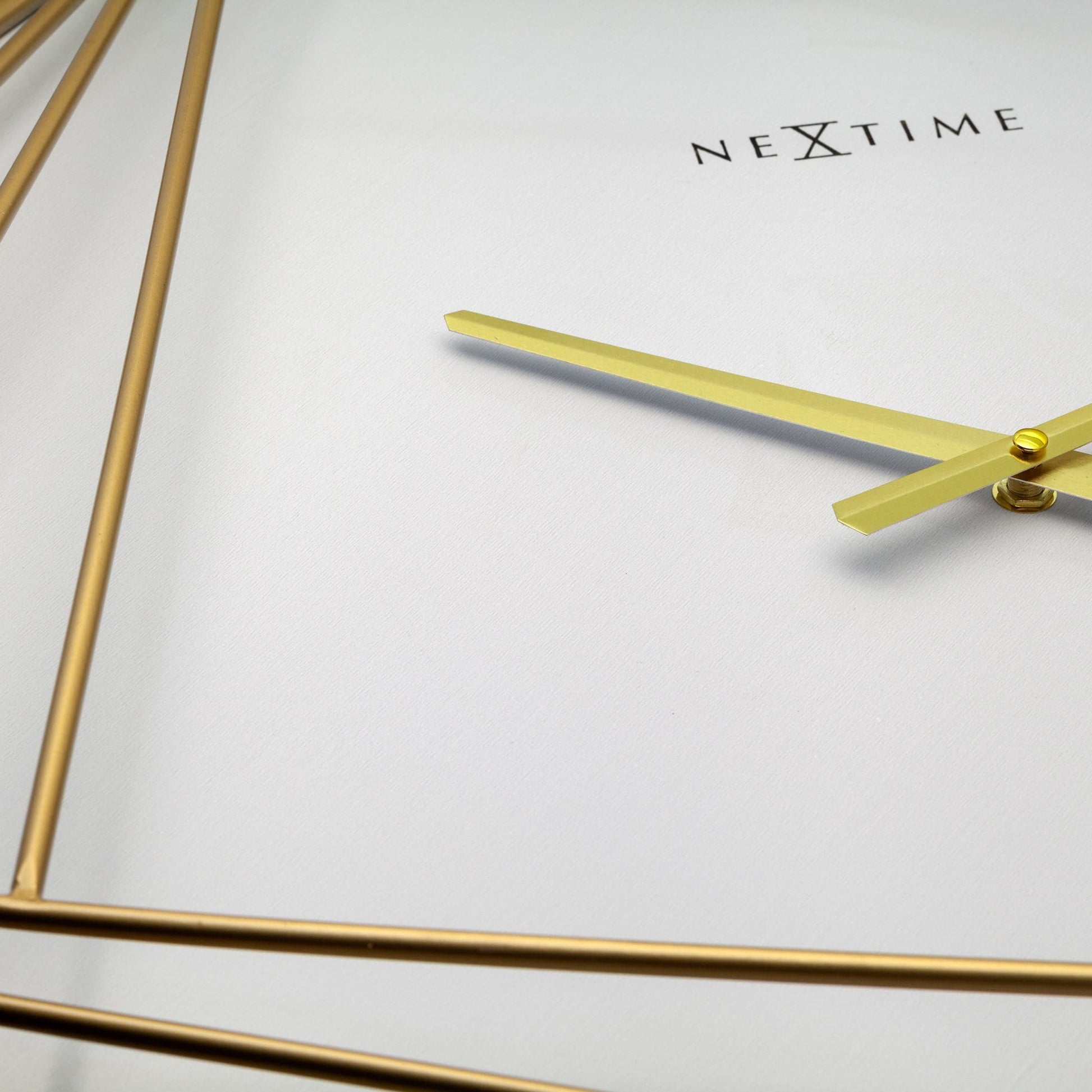 Een elegante, goudkleurige wandklok met geometrische lijnen en een witte wijzerplaat. De minimalistische klok heeft dunne wijzers en het merk 'NEXTIME' zichtbaar, perfect voor moderne interieurs en als decoratief element in woon- of kantoorruimtes.