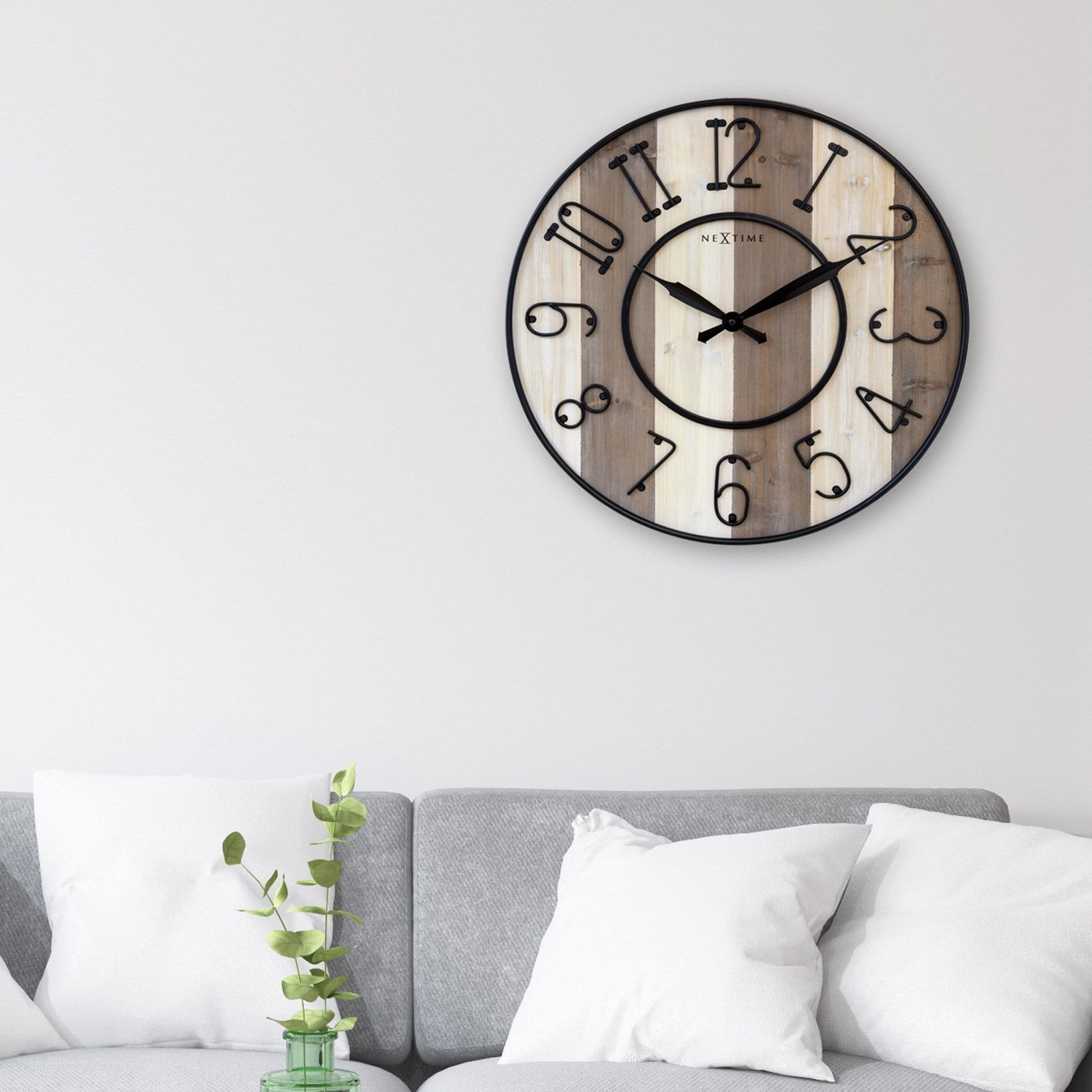 Een ronde wandklok van Nextime met een houten oppervlak in licht- en donkergrijs, zwarte metalen cijfers en wijzers. Geschikt voor moderne interieurs en als decoratief element in woon- of kantoorruimtes.