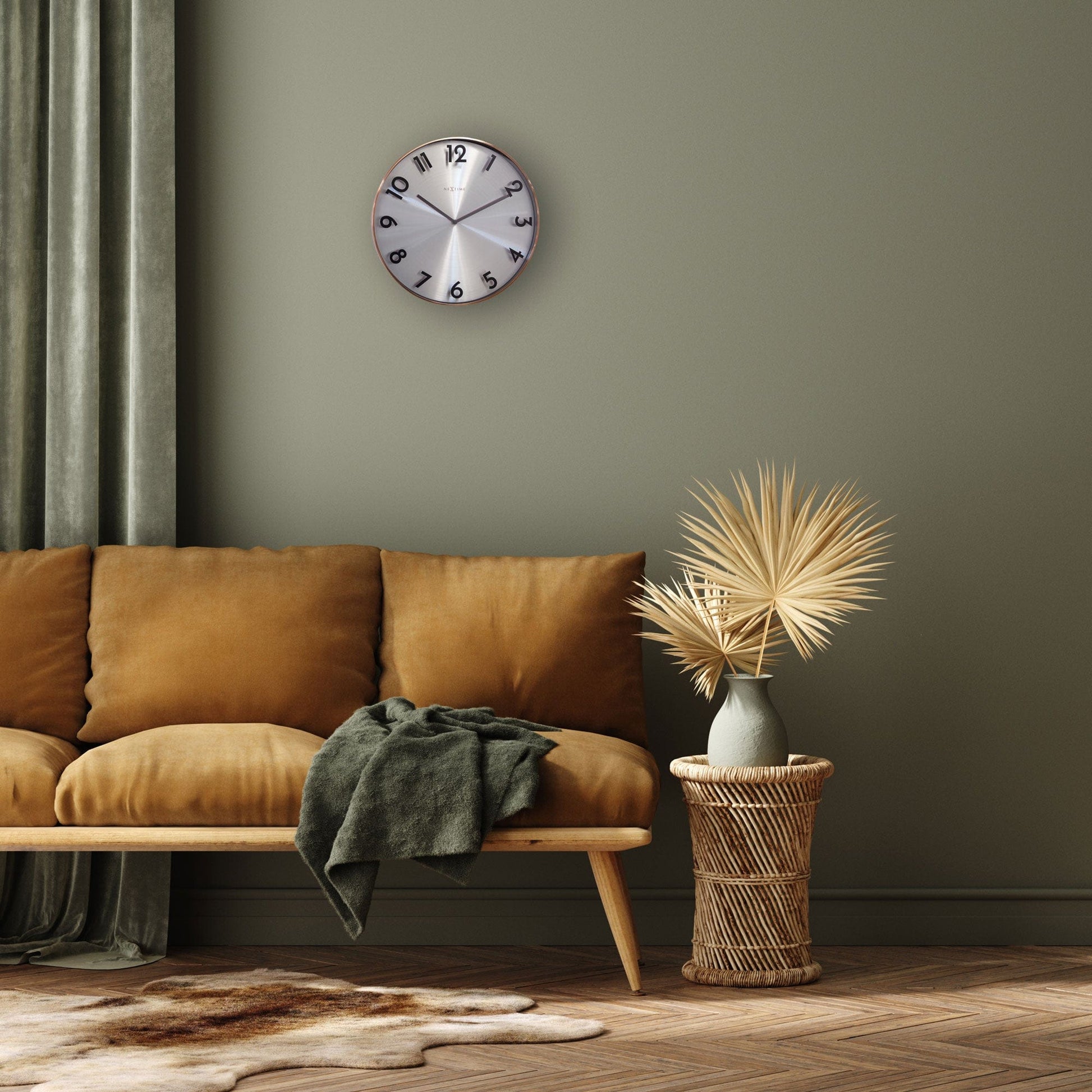 Een moderne wandklok met zilverkleurig, geborsteld wijzerplaat en zwarte cijfers, omlijst met een warme koperen rand. Geschikt voor minimalistische interieurs en als decoratief element in woon- of kantoorruimtes.