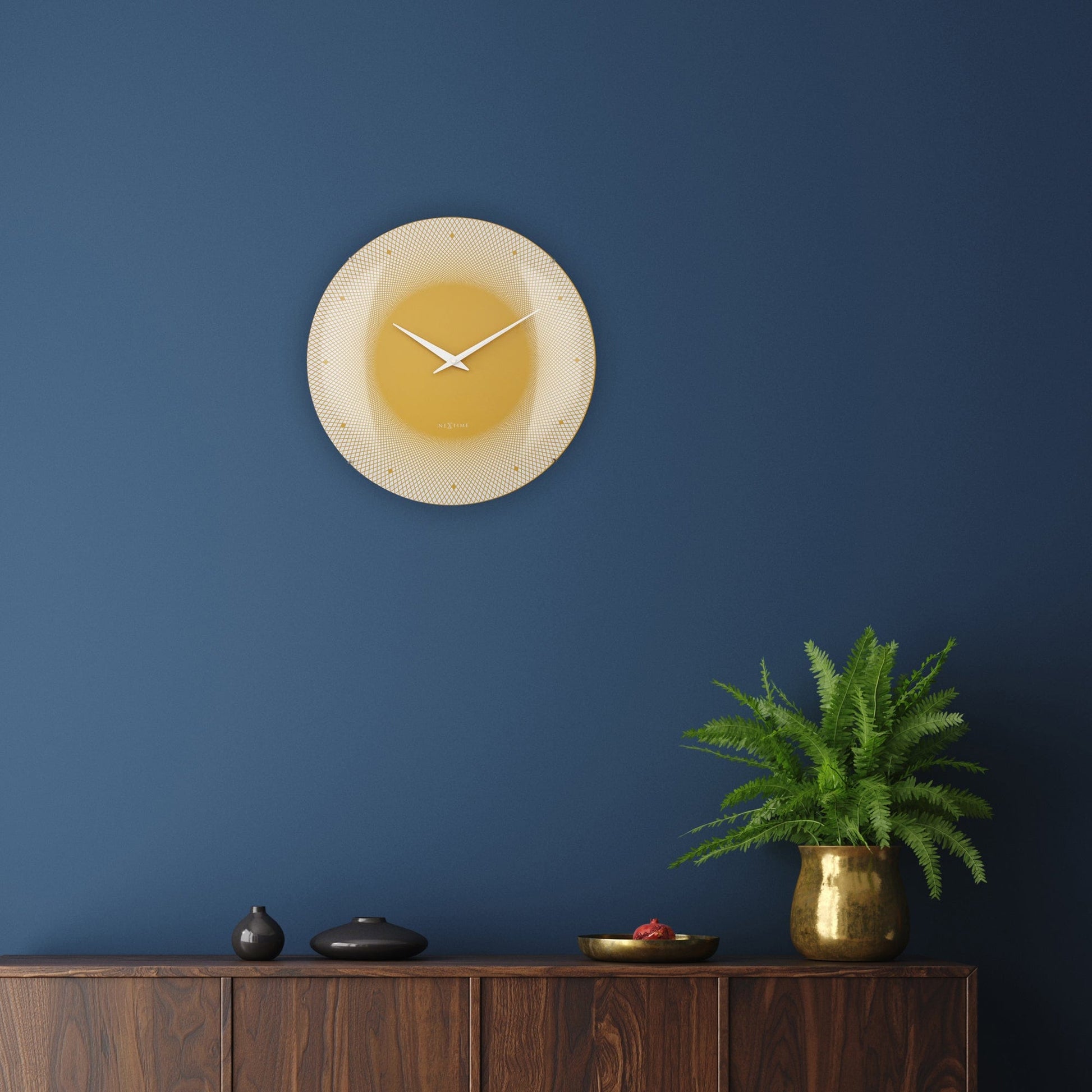 Een moderne wandklok in warme goudkleur met witte wijzers en een geometrisch patroon. Geschikt voor woonkamer of kantoor, met minimalistisch design en het merk NEXtime.