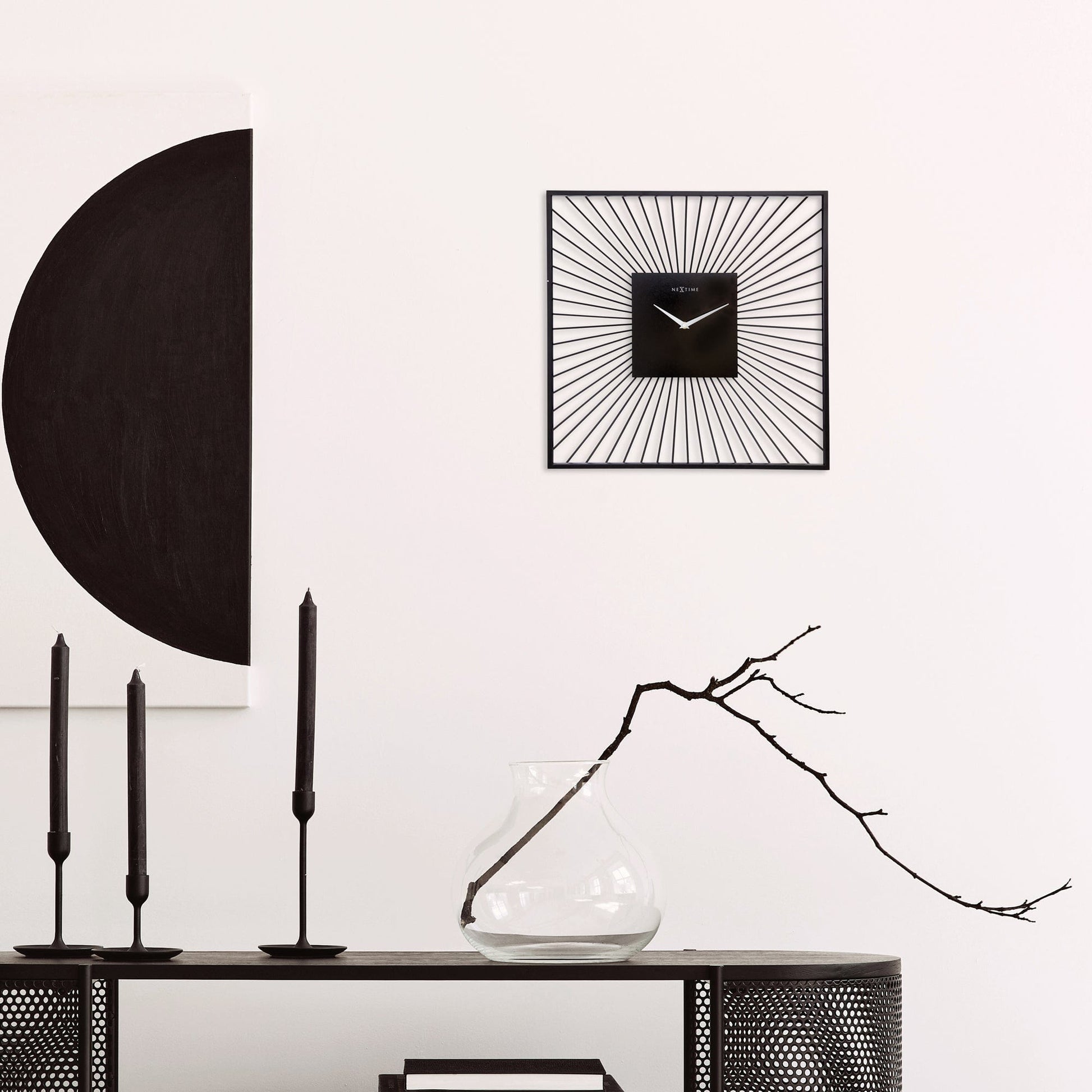 Een zwart, minimalistisch wandklok met zonnestraalontwerp en witte wijzers. Geschikt voor moderne interieurs, met zichtbare merknaam NEXTIME op het klokgezicht.