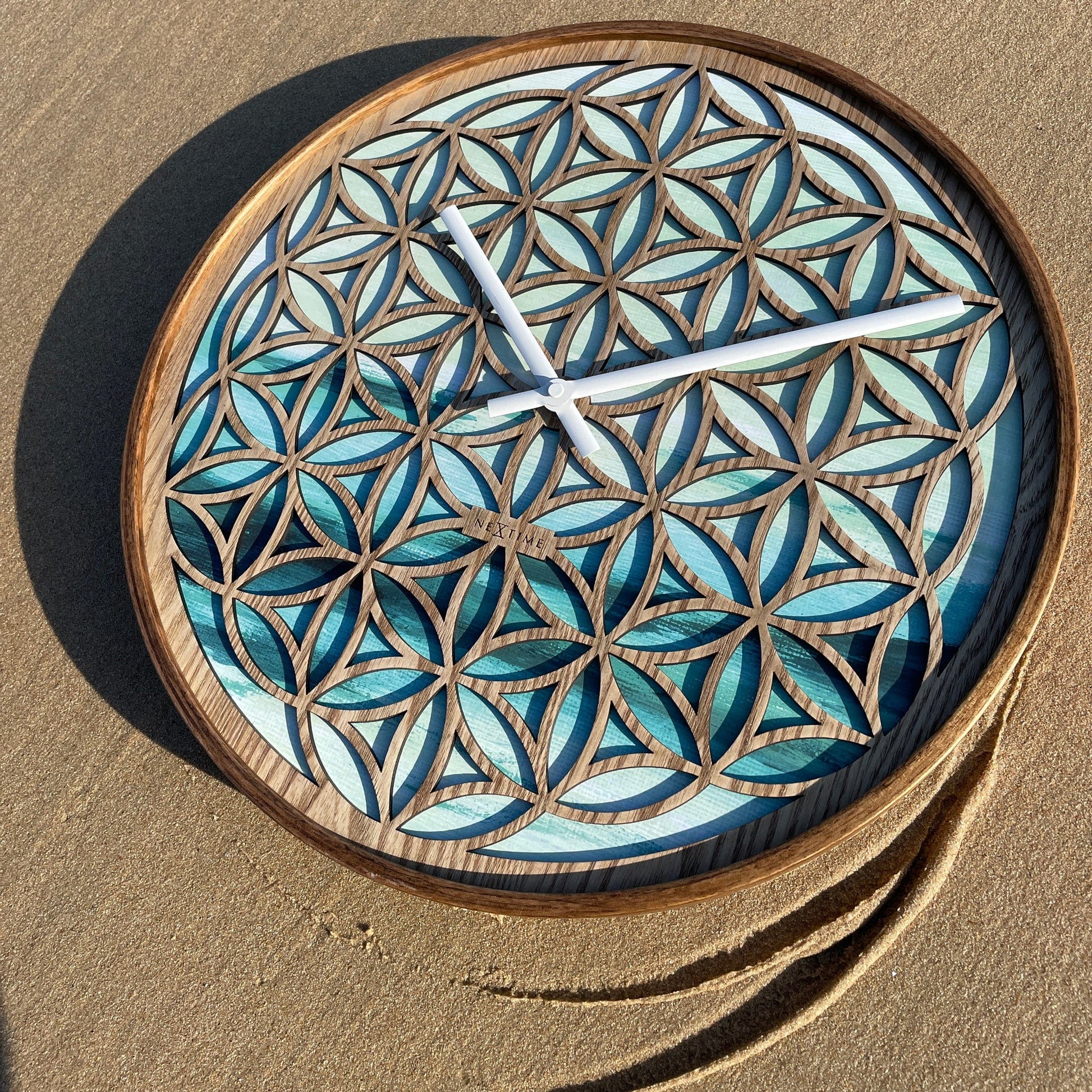 Een houten wandklok met bloem van leven patroon, blauwe glaspanelen en witte wijzers. Perfect voor een zen- of meditatieruimte, met natuurlijk hout en kalmerende kleuren.