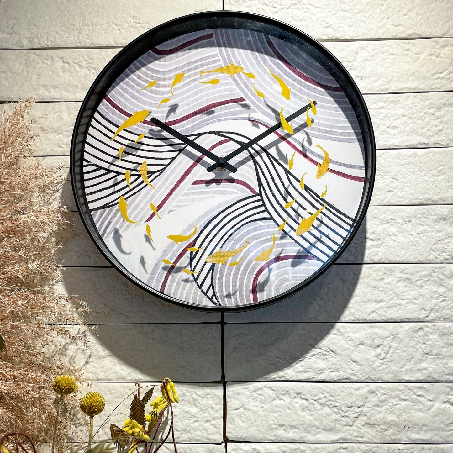 Een ronde wandklok met zwart frame en een kunstwerk van gouden vissen op gestreepte golven. Perfect voor een moderne woonkamer of kantoordecoratie met een artistieke touch.
