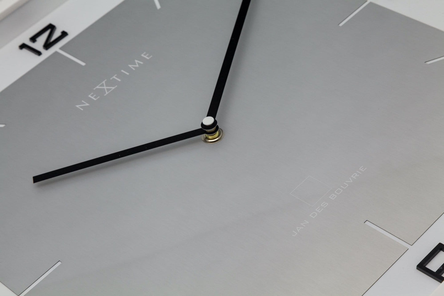 Een minimalistische, zilverkleurige wandklok met zwarte cijfers en wijzers, in een witte rand. Geschikt voor moderne interieurs en kantoorruimtes, met een strak design voor tijdweergave.