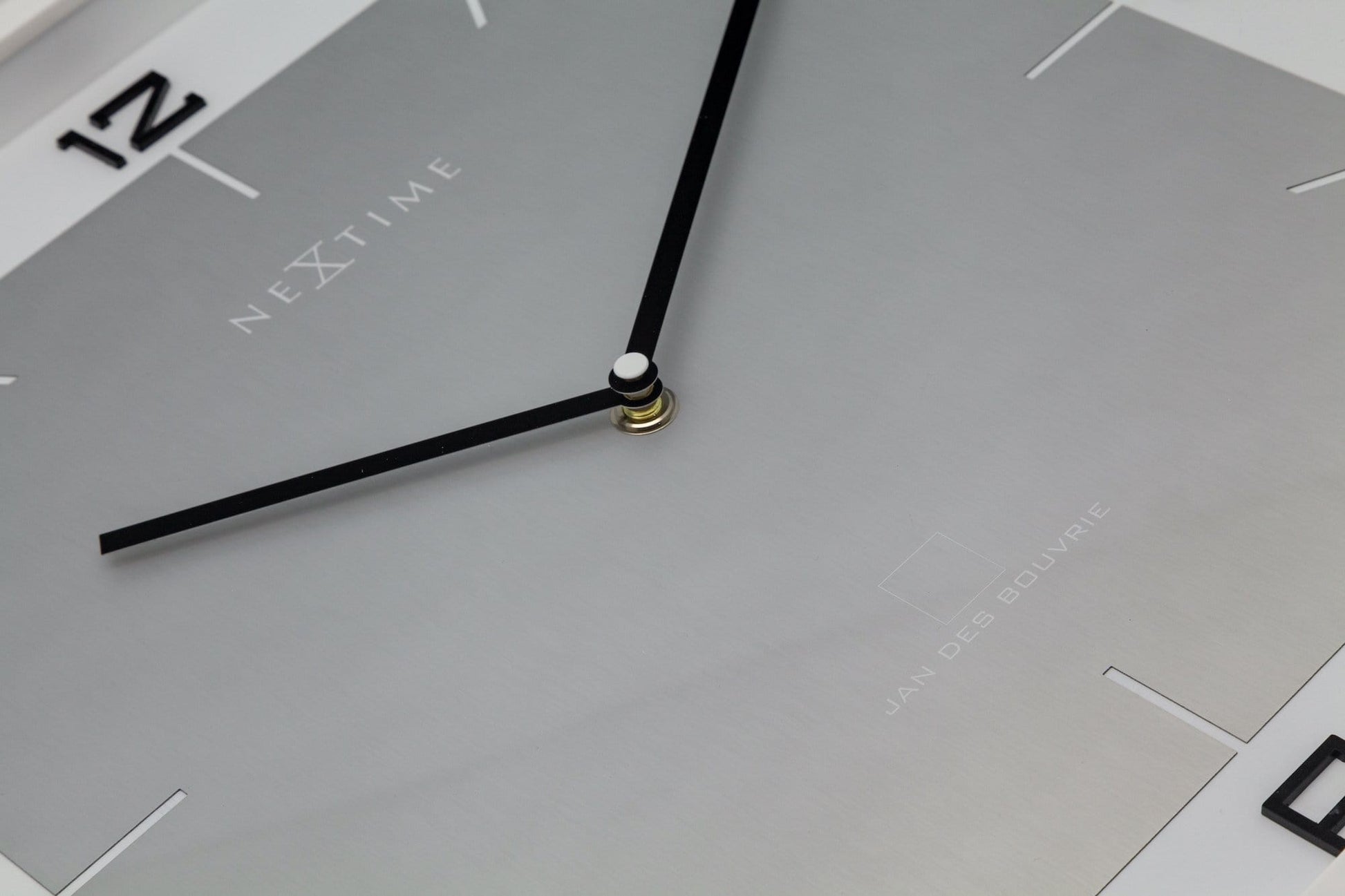 Een minimalistische, zilverkleurige wandklok met zwarte cijfers en wijzers, in een witte rand. Geschikt voor moderne interieurs en kantoorruimtes, met een strak design voor tijdweergave.