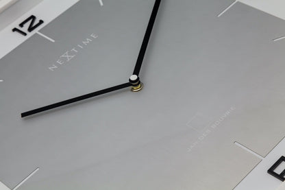 Een minimalistische, zilverkleurige wandklok met zwarte cijfers en wijzers, in een witte rand. Geschikt voor moderne interieurs en kantoorruimtes, met een strak design voor tijdweergave.