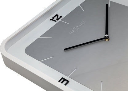 Een minimalistische, zilverkleurige wandklok met zwarte cijfers en wijzers, in een witte lijst. Geschikt voor moderne interieurs en als decoratief element in woon- of kantoorruimtes.