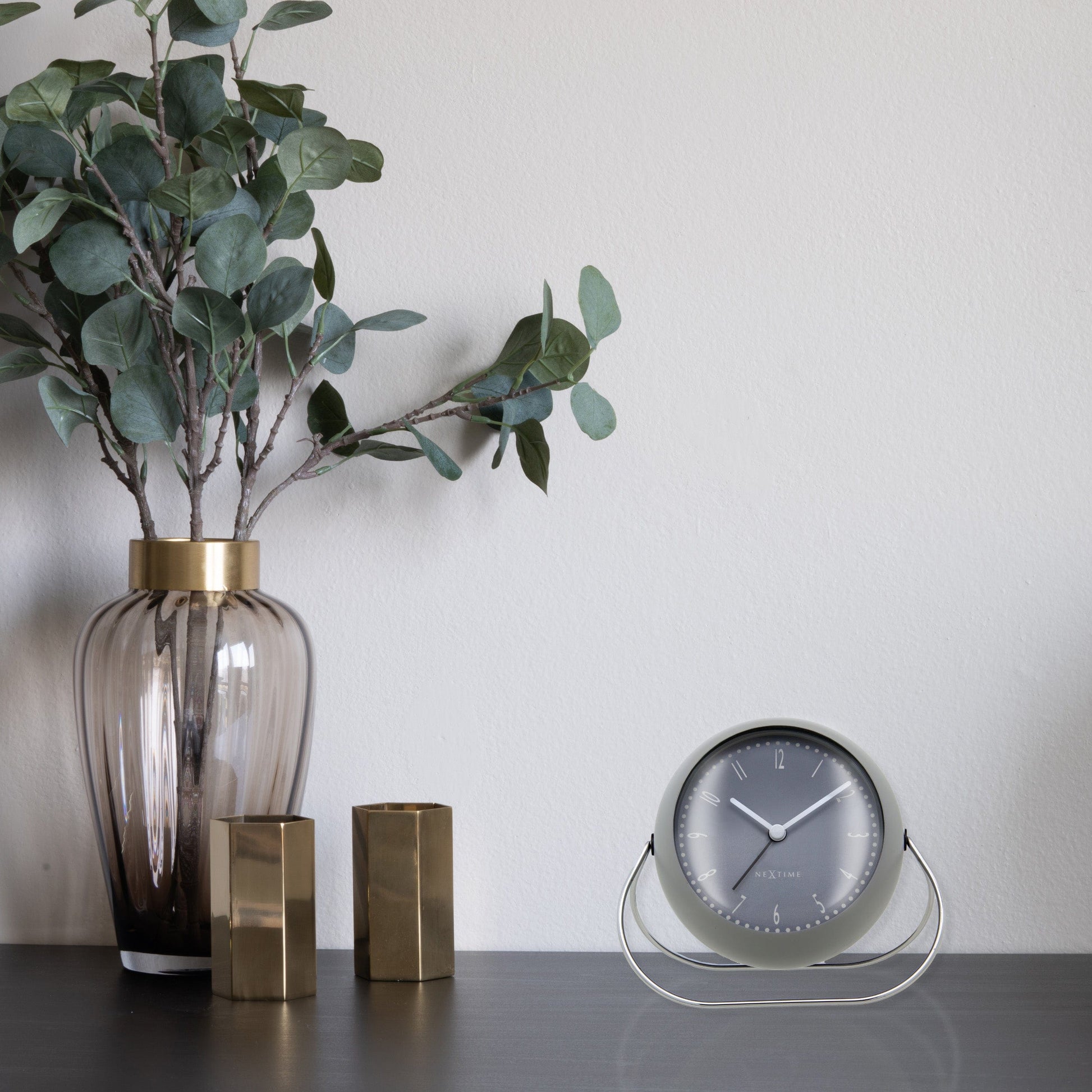Een zwarte, ronde wekker van het merk Nextime met een zilverkleurig wijzerplaatje en zwarte wijzers. Geschikt voor kantoor of thuis, met een minimalistisch design voor moderne interieurs.