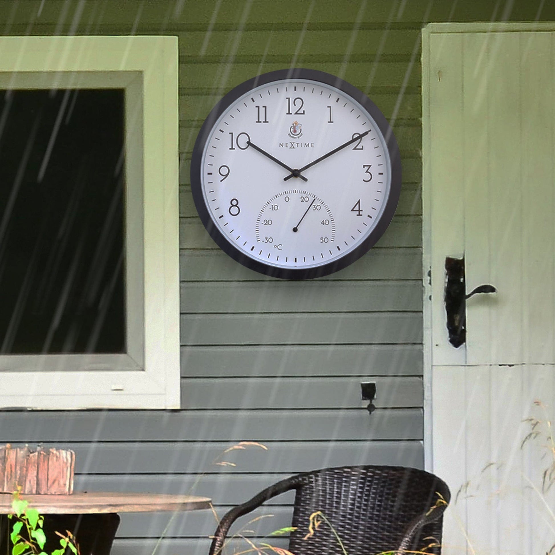 Een zwarte wandklok van NEXtime met witte wijzerplaat en duidelijke cijfers, inclusief een temperatuurindicatie van -30 tot 50 graden Celsius, geschikt voor kantoor of huis.