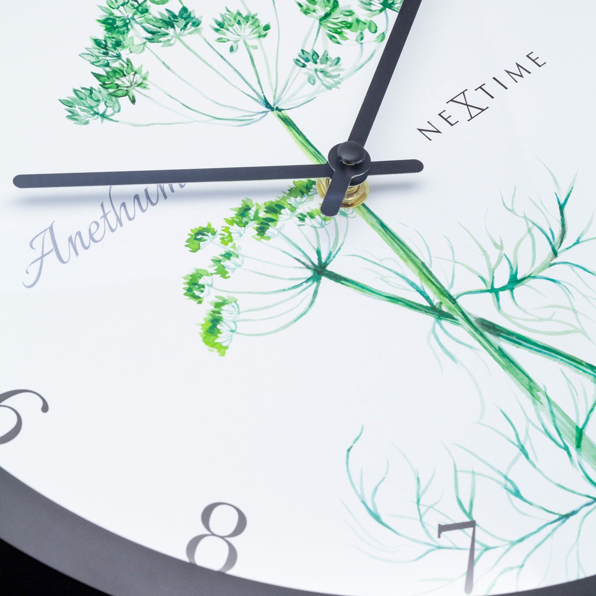 Een wandklok met zwart kader en witte wijzerplaat, versierd met een groene anethoontje-illustratie. De wijzers en cijfers zijn zwart, met het merk 'NEXtime' zichtbaar. Perfect voor een natuurlijke, decoratieve klok in de keuken of woonkamer.