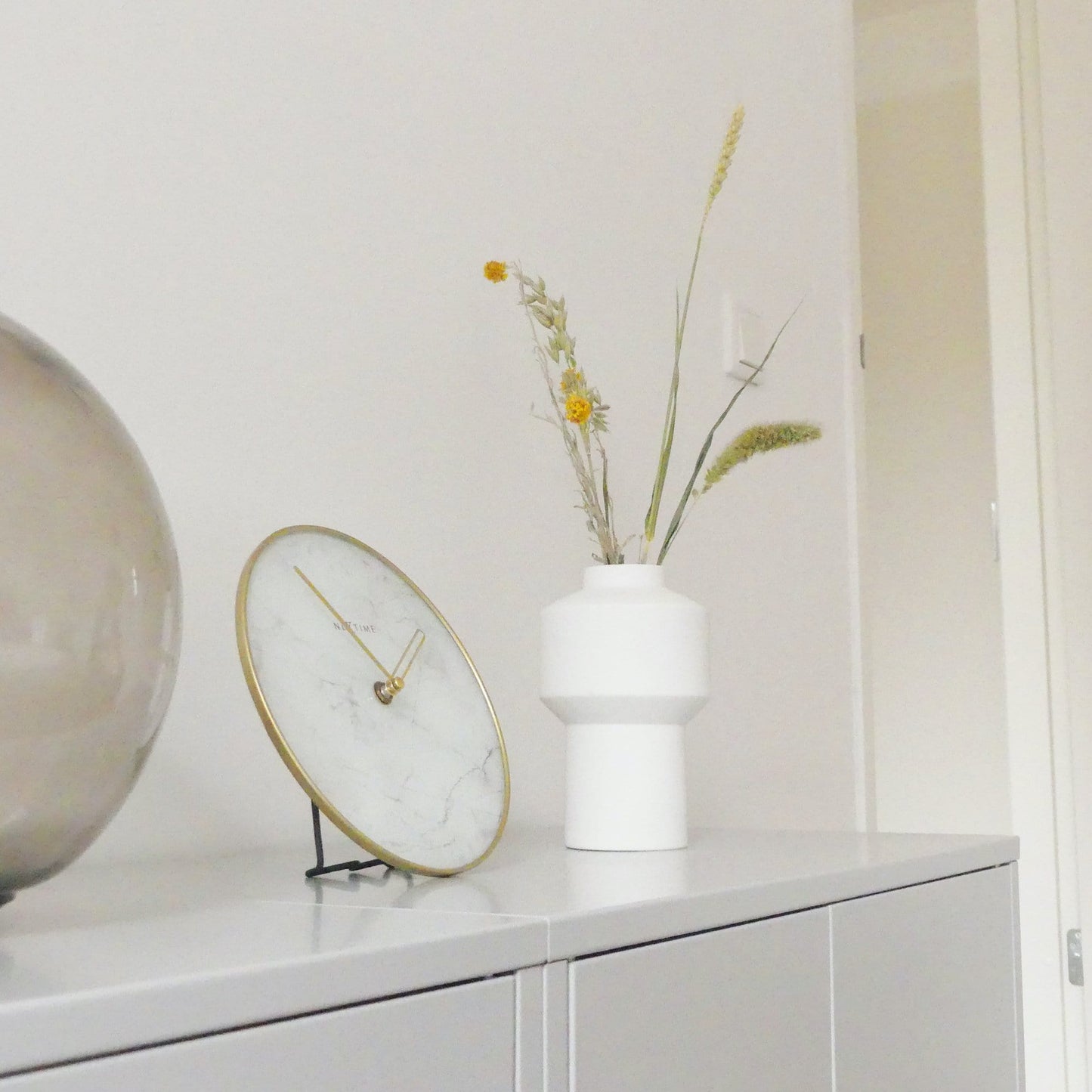 Een elegante wandklok met wit marmeren wijzerplaat en goudkleurige wijzers, omlijst door een goudkleurige metalen rand. Geschikt voor moderne interieurs en kantoorruimtes met minimalistische stijl.