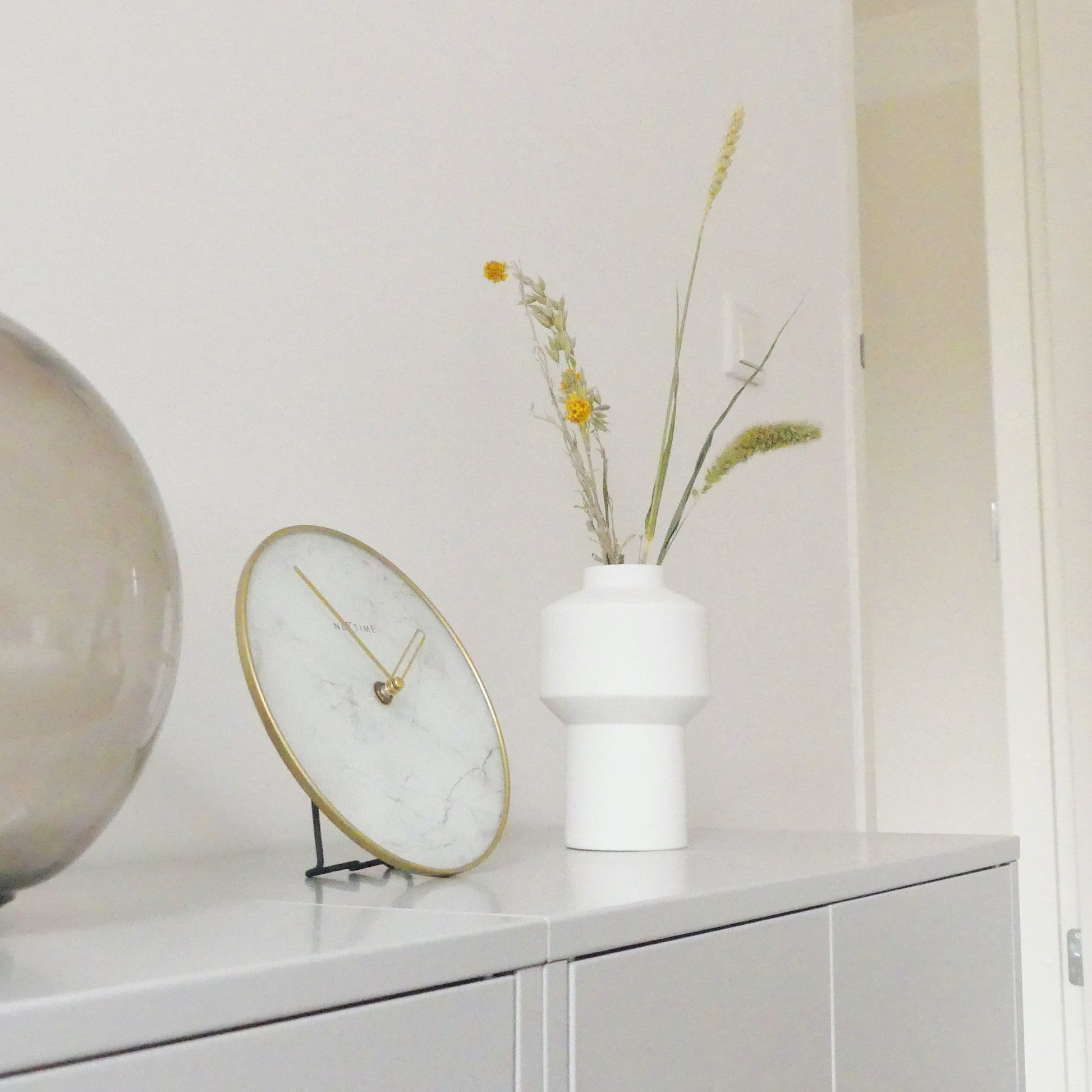 Een elegante wandklok met wit marmeren wijzerplaat en goudkleurige wijzers, omlijst door een goudkleurige metalen rand. Geschikt voor moderne interieurs en kantoorruimtes met minimalistische stijl.